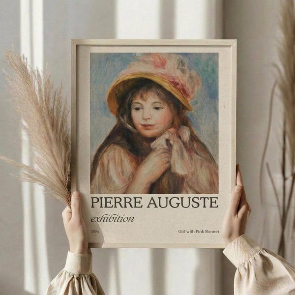 May include: Hands holding a framed exhibition poster featuring a soft impressionist painting of a young girl wearing a yellow hat with pink ribbons. The artwork shows warm, muted tones with the girl's gentle expression and flowing hair. Dried wheat stalks are visible on the left side, and the person wears a cream-colored ruffled sleeve top against white curtains in soft natural lighting.