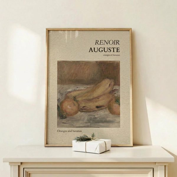 May include: Framed museum-style poster featuring Renoir's still life painting of oranges and bananas in warm earth tones, displayed on light wood surface next to small white wrapped gift with evergreen sprig, set against cream colored wall with natural lighting