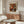 May include: Warm wood sideboard with white table lamp and framed vintage floral poster showing orange and white chrysanthemums in blue-striped vase. Modern living room setting features cream sculptural chair, glass oval coffee table, and neutral walls. Poster displays in thin wood frame above mid-century furniture.