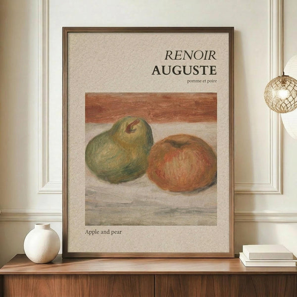 May include: Framed art print displaying Renoir's painting of a green pear and red apple on a beige background, positioned on a wooden sideboard next to a white ceramic vase and books, with a woven pendant light visible in an elegant room setting with cream walls and decorative molding.