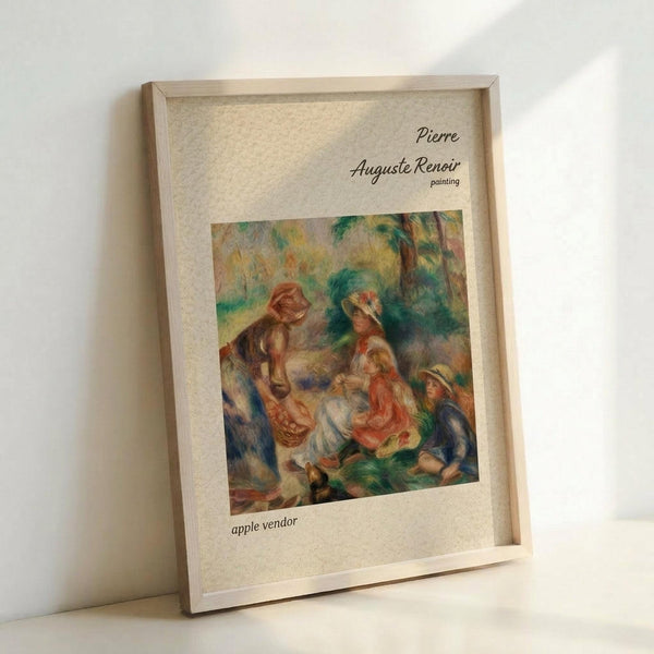 May include: Framed art print leaning against white wall showing Renoir's impressionist painting of people in a pastoral scene with warm colors of orange, green, and yellow. The wooden frame surrounds a cream-colored mat with black text identifying the artist and artwork title. Soft natural lighting creates gentle shadows on the wall behind the rectangular frame.
