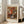 May include: Framed art print of Renoir's impressionist flower painting showing vibrant orange, red, and white blooms in a blue and white ceramic vase. The poster features "BOUQUET" at top and "PIERRE AUGUSTE RENOIR 1919" at bottom on cream background with thin wooden frame, leaning against white wall next to beige upholstered chair in bright, naturally lit room with hardwood floors.