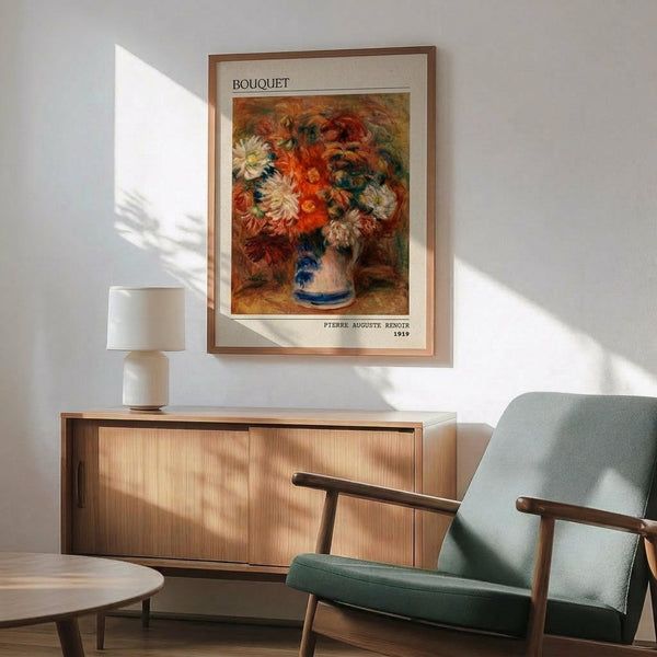 May include: Framed art print of Renoir's colorful floral bouquet painting from 1919, featuring vibrant orange, red, and white flowers in a blue and white ceramic vase. The poster hangs above a mid-century modern wooden credenza with a white table lamp. A sage green upholstered armchair with wooden frame sits nearby, with warm sunlight casting geometric shadows across the white wall and wooden floor.