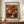 May include: Framed reproduction print of Renoir's impressionist flower painting featuring vibrant orange, red and white blooms in a blue-striped ceramic vase. The poster has "BOUQUET" at top and "PIERRE AUGUSTE RENOIR 1919" at bottom on cream matting with brown frame. Displayed on wooden sideboard next to white ceramic vase and books in elegant room with white wainscoting.