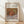 May include: Framed art print displaying Renoir's impressionist still life painting of pomegranates in warm reddish-brown tones with green fruit, mounted in light wood frame against cream textured wall on wooden floor with soft natural lighting and shadows