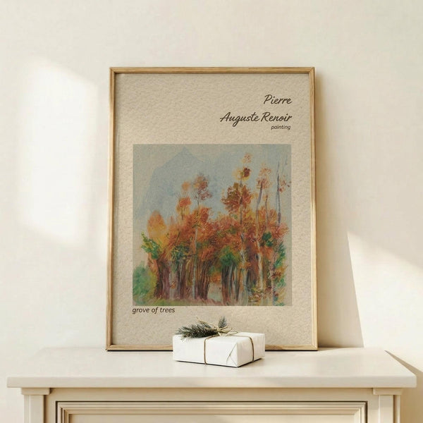 May include: Framed art print displaying Pierre Auguste Renoir's impressionist painting of autumn trees with orange and green foliage against a pale blue sky. Print has cream matting with text identifying the artist and artwork title. Natural wood frame sits on light wooden surface alongside small white wrapped gift with evergreen sprig and twine. Soft shadows cast on neutral beige wall behind.