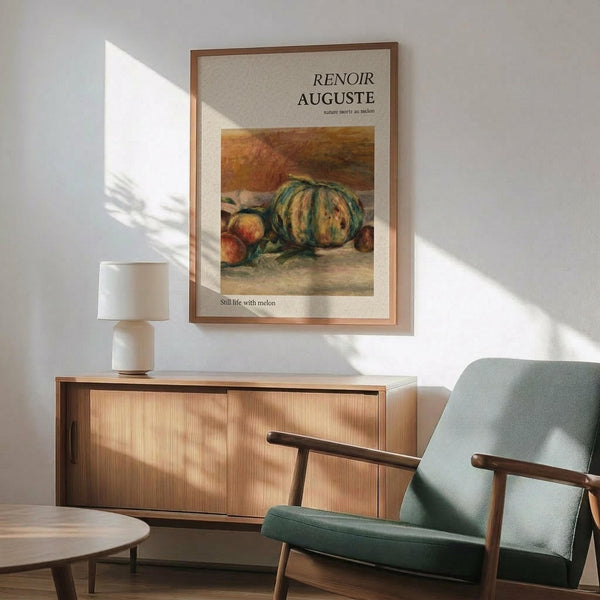 May include: Framed art print featuring Auguste Renoir's still life painting of a green striped melon and peaches in warm earth tones, displayed above a mid-century modern wooden sideboard with white ceramic lamp. The poster has cream matting in a thin wood frame, positioned in a minimalist room setting with sage green upholstered armchair, round coffee table, and natural sunlight casting geometric shadows on white walls.