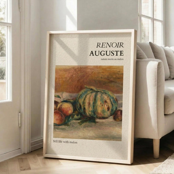May include: Framed art print featuring a Renoir still life painting of striped melons and fruit in warm earth tones, displayed on light wooden floors against white walls next to a beige upholstered sofa. The cream-colored frame contains exhibition-style text above and below the impressionist artwork showing green and yellow striped melons with peaches.