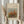 May include: Person in cream ruffled sleeve top holding framed art print featuring Renoir's autumn grove of trees painting with orange and green foliage, displayed in natural wood frame with cream matting, alongside dried wheat stalks against soft neutral curtained background.