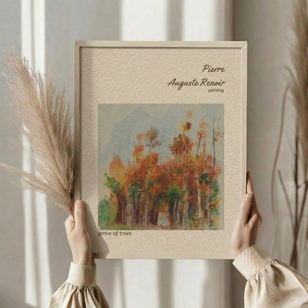 May include: Person in cream ruffled sleeve top holding framed art print featuring Renoir's autumn grove of trees painting with orange and green foliage, displayed in natural wood frame with cream matting, alongside dried wheat stalks against soft neutral curtained background.