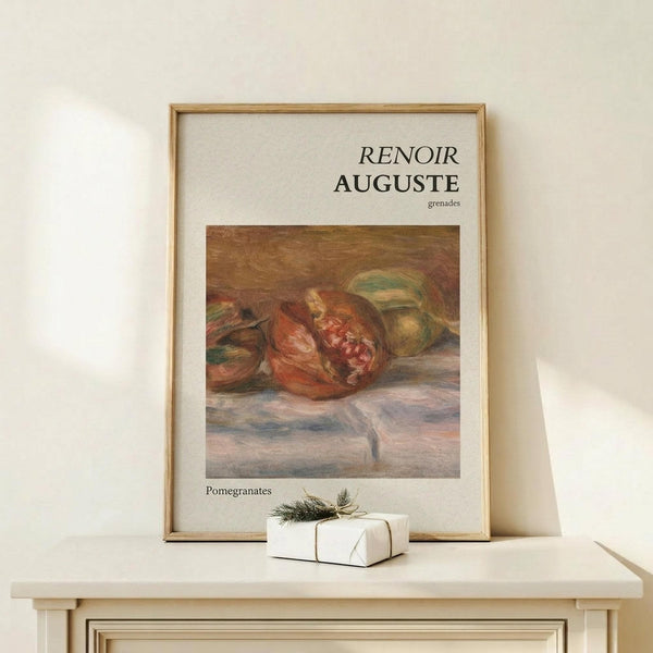 May include: Framed art print displaying Renoir's impressionist still life painting of ripe pomegranates in warm red and orange tones against muted background, positioned on light wood console table beside small white wrapped gift with evergreen sprig, against cream colored wall with natural lighting