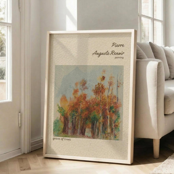 May include: Framed art print featuring Pierre Auguste Renoir's impressionist painting of autumn trees in warm oranges, reds, and greens against a soft blue sky. The beige matted poster displays in a light wood frame, leaning against a beige upholstered chair in a bright room with white walls and large windows casting natural light across light hardwood floors.