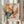 May include: Person holding framed abstract expressionist poster with colorful paint splatters and drips in blue, orange, yellow, pink and black on cream background, standing near dried pampas grass against white curtained window