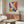 May include: Colorful abstract art poster with vibrant paint splatters in blues, oranges, purples, and yellows displayed in thin gold frame above modern walnut credenza. White sculptural chair and glass-top oval coffee table visible in minimalist living room with cream walls and natural lighting.