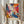 May include: Person in cream sweater holding framed abstract art print with vibrant paint splatters and swirls in blues, oranges, purples, and yellows. Dried pampas grass visible to left, soft beige curtains in background. Poster features bold gestural brushstrokes and drip painting technique with "POLLOCK" text below artwork.