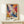 May include: Framed abstract art poster with vibrant swirling paint in blues, oranges, purples, and yellows against white background, displayed on light wood console table next to small wrapped gift with twine and greenery sprig