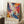 May include: Framed abstract expressionist art print with vibrant swirling colors in blues, oranges, purples, and yellows against white background, displayed leaning against white wall corner next to wooden side table with white coffee cup and saucer, positioned on light textured rug beside beige fabric furniture.