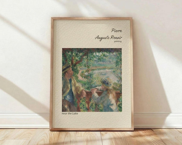 May include: Framed art print featuring Pierre-Auguste Renoir's impressionist painting showing figures relaxing by a lake surrounded by lush green foliage. The artwork displays soft brushstrokes in greens, blues, and earth tones within a light wood frame against cream matting. The poster leans against a white wall on light wooden flooring with natural sunlight casting diagonal shadows across the scene.