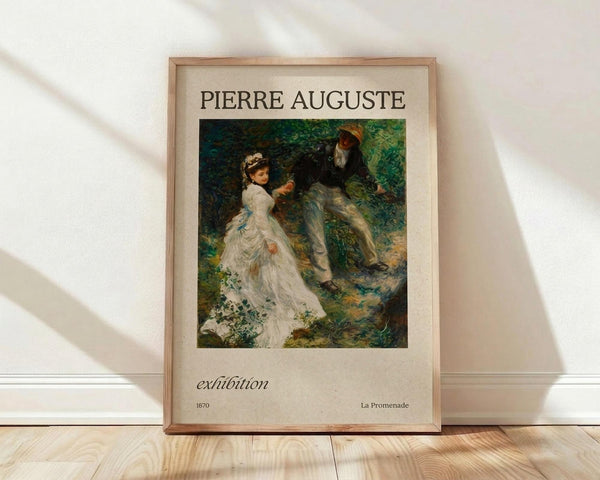 May include: Framed vintage exhibition poster featuring Pierre-Auguste Renoir's "La Promenade" from 1870, showing a woman in white dress and man in dark clothing walking through dappled forest sunlight. The cream-colored poster with elegant typography sits against white fabric backdrop on light wood flooring, with soft natural lighting creating diagonal shadows.