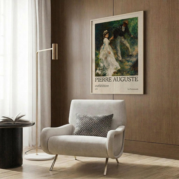 May include: A framed poster featuring an impressionist painting of a man and woman in 19th-century dress walking through a lush green forest. The woman wears a flowing white dress and the scene has soft, dappled lighting. The poster displays "PIERRE AUGUSTE" and "exhibition" text below the artwork. Shown in a modern living room setting with a beige upholstered armchair, geometric patterned pillow, brass floor lamp, and wood-paneled wall.