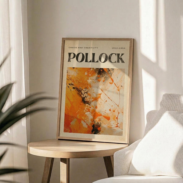 May include: Framed art poster featuring Jackson Pollock's abstract expressionist painting in vibrant orange, yellow, black and white paint splatters and drips, displayed on a light wood round side table next to a beige upholstered chair with green plant leaves visible, natural sunlight casting shadows across white walls in a minimalist modern living room setting.