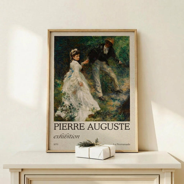 May include: Framed exhibition poster featuring Renoir's impressionist painting of a couple in a forest setting - woman in flowing white dress with blue sash, bearded man in dark clothing and cap. Poster displays "PIERRE AUGUSTE exhibition" text with "1870" and "La Promenade" details. Natural wood frame sits on light wooden surface next to small white wrapped gift with twine and greenery against cream wall.