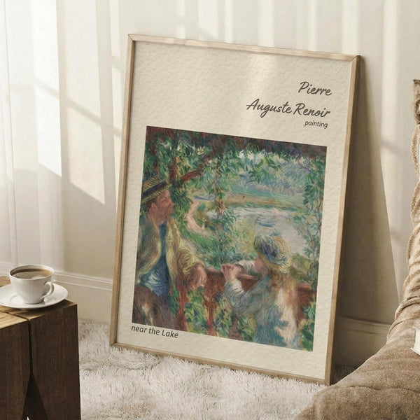 May include: Framed art print of an impressionist landscape painting leaning against white wall corner. The artwork shows figures near water with lush green foliage and soft brushstrokes in blues, greens, and earth tones. Cream matting surrounds the image with artist attribution text. A coffee cup sits on wooden block nearby, with textured cream rug and beige throw blanket visible.