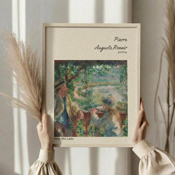 May include: Person in beige clothing holding framed reproduction of Impressionist painting showing figures near water surrounded by lush greenery in soft blues, greens, and earth tones. Light wood frame with cream matting against neutral curtained background. Dried wheat stems visible on left side.