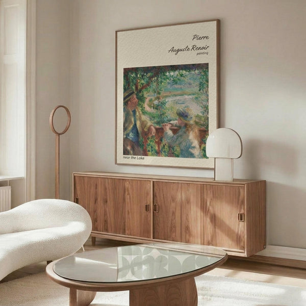 May include: A framed Renoir reproduction print displayed above a mid-century modern wooden credenza in a minimalist living room. The impressionist artwork features soft pastels depicting figures near a lake with lush green foliage. The room has neutral beige walls, a white curved chair, glass-top oval coffee table, and sleek brass floor and table lamps creating warm ambient lighting.