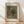 May include: Framed art print leaning against white wall on light wood floor. Shows Pierre Auguste Renoir's 1866 floral still life painting featuring colorful wildflowers - red, blue, white, and yellow blooms - arranged in an earthenware vase on a table. The reproduction has a muted, classical color palette with soft lighting. Displayed in thin wooden frame with cream matting.