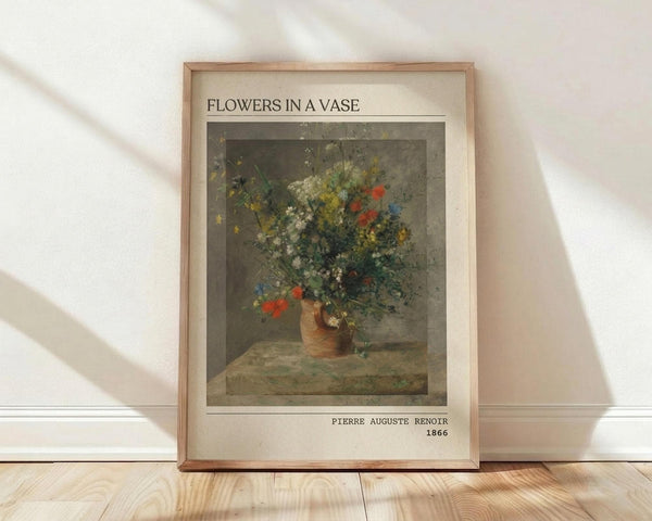 May include: Framed art print leaning against white wall on light wood floor. Shows Pierre Auguste Renoir's 1866 floral still life painting featuring colorful wildflowers - red, blue, white, and yellow blooms - arranged in an earthenware vase on a table. The reproduction has a muted, classical color palette with soft lighting. Displayed in thin wooden frame with cream matting.