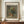 May include: Framed vintage-style poster print featuring Impressionist wildflower bouquet in earthenware vase, displayed on wooden sideboard with white ceramic vase and books in elegant room with cream walls and white molding.
