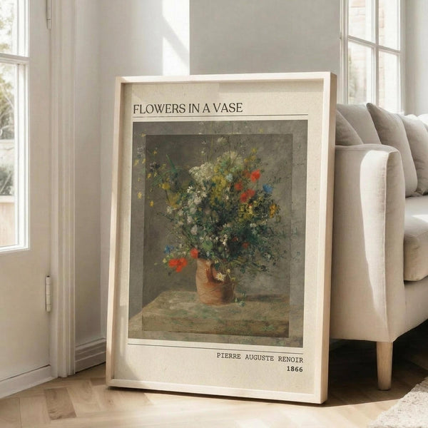 May include: Framed art print leaning against beige sofa in bright living room with white walls and windows. Print shows impressionist-style floral still life painting with wildflowers in earthenware vase, featuring red, blue, yellow and white blooms against muted gray-green background. White matted frame with museum-style text labels above and below artwork.