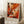 May include: Framed abstract art poster with vibrant orange, red, and black paint splatters in expressive brushstroke style, leaning against white wall corner. White coffee cup on wooden block nearby, beige textured rug below, soft natural lighting creating gentle shadows across the scene.