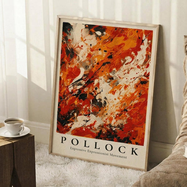 May include: Framed abstract art poster with vibrant orange, red, and black paint splatters in expressive brushstroke style, leaning against white wall corner. White coffee cup on wooden block nearby, beige textured rug below, soft natural lighting creating gentle shadows across the scene.