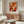 May include: Abstract expressionist art print with vibrant orange, red, and black paint splatters displayed in thin wooden frame above walnut credenza in modern living room. White sculptural chair and glass oval coffee table complete the minimalist scene with natural lighting casting soft shadows on cream walls.