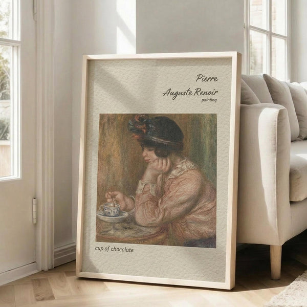 May include: Framed art print leaning against beige couch in sunlit living room with hardwood floors and white walls. The poster features Renoir's painting of a woman in pink dress and dark hat holding a teacup, with vintage-style text layout on cream textured background within light wood frame.