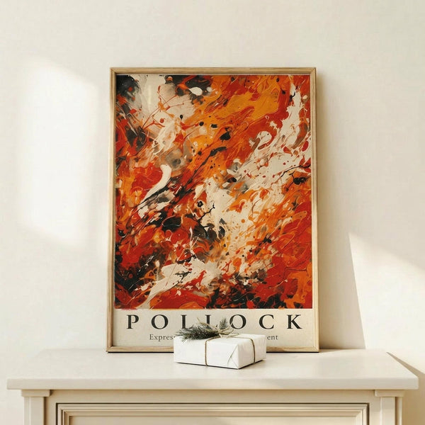 May include: Framed abstract expressionist artwork in warm orange, red, and black paint splatters and brushstrokes, displayed on white wooden console table against cream wall. Small white gift box with evergreen sprig sits beside the light wood frame.