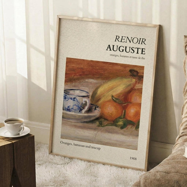 May include: Framed art print leaning against white wall on textured white rug. The poster features a Renoir still life painting showing oranges, bananas, and a blue and white patterned teacup on wooden surface. Light wooden frame with cream matting. Small wooden side table with white coffee cup visible on left. Soft natural lighting creates gentle shadows on the wall.