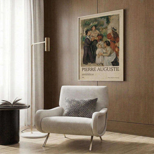 May include: Beige armchair with geometric patterned pillow positioned next to wood paneled wall displaying framed exhibition poster featuring Renoir's colorful family portrait painting. Modern floor lamp with brass finish and circular white base stands nearby. Natural lighting from window with curtains creates warm, contemporary living room setting.