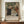 May include: Framed exhibition poster featuring Renoir's 1896 painting of a family group with adults and children in period clothing, displayed on wooden sideboard next to white ceramic vase and books against cream walls with white molding in elegant interior setting.