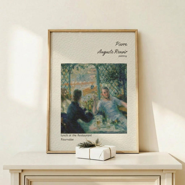 May include: Framed art print of Renoir's impressionist painting showing people dining at a restaurant, with soft blue and green tones. The cream-colored poster features black text identifying the artist and artwork title. Natural wood frame sits on a light wooden surface next to a small white wrapped gift with twine and greenery against a neutral wall.