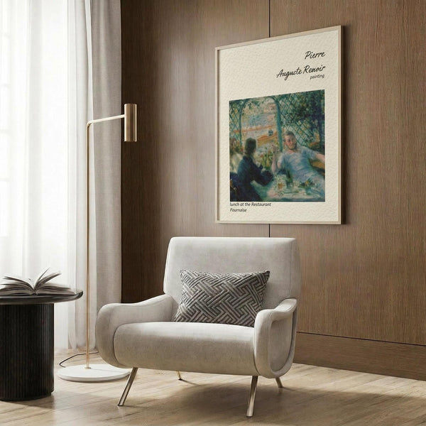 May include: A framed Renoir poster print hanging on wood paneled wall above a beige armchair with geometric pillow. The vintage-style art poster shows an impressionist restaurant scene with people dining outdoors in soft blues and greens. Modern brass floor lamp and black side table with open book complete the neutral-toned reading nook setting.