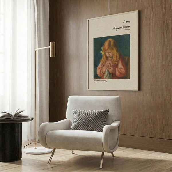 May include: Framed Renoir poster print showing red-haired girl in coral dress sewing, mounted on wood panel wall above beige upholstered armchair with geometric pillow. Modern brass floor lamp and black side table with open book complete the neutral-toned living room scene with wood flooring and white curtains.