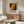 May include: Abstract art poster with Jackson Pollock-style paint splatters in orange, yellow, black and red tones, displayed in thin wooden frame above mid-century modern walnut credenza. Room features white curved chair, oval glass coffee table, brass floor lamp, and minimalist decor in neutral tones with natural lighting.