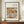 May include: Framed art print featuring Renoir's impressionist painting of three pears on white fabric, displayed on wooden sideboard beside white ceramic vase and stacked books against cream paneled wall in elegant interior setting.