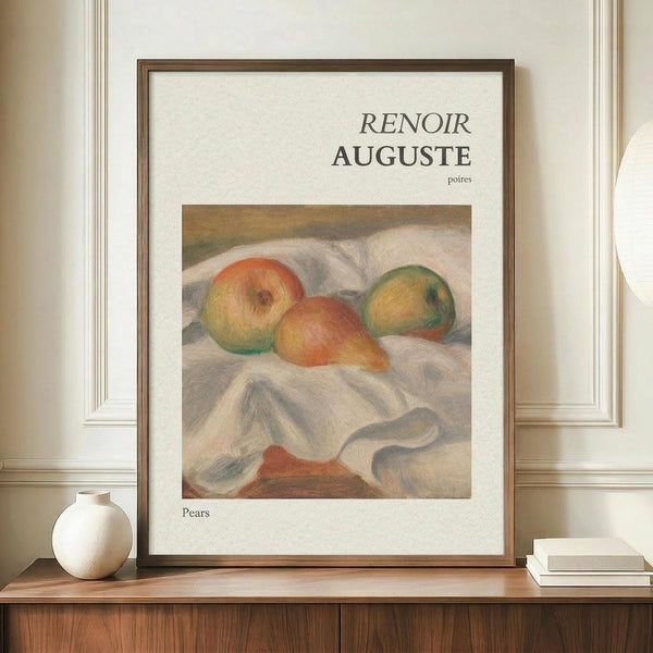 May include: Framed art print featuring Renoir's impressionist painting of three pears on white fabric, displayed on wooden sideboard beside white ceramic vase and stacked books against cream paneled wall in elegant interior setting.