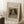 May include: Framed reproduction of Renoir's 1870 dog portrait displayed in cozy room setting. The artwork shows a small long-haired dog with dark ears wearing a collar with pendant, rendered in warm brown tones. Light wooden frame with cream matting leans against white wall near wooden side table with coffee cup and soft beige throw blanket on textured white rug.