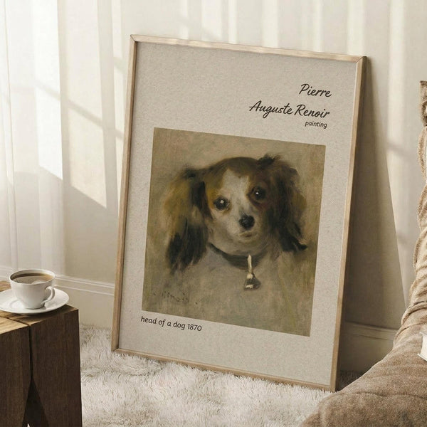 May include: Framed reproduction of Renoir's 1870 dog portrait displayed in cozy room setting. The artwork shows a small long-haired dog with dark ears wearing a collar with pendant, rendered in warm brown tones. Light wooden frame with cream matting leans against white wall near wooden side table with coffee cup and soft beige throw blanket on textured white rug.