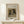 May include: Framed art print of a small dog with brown and white fur and dark ears wearing a collar, displayed on a light wooden console table next to a wrapped white gift box with evergreen sprig. The vintage-style painting reproduction is mounted in a thin wooden frame with cream matting against a soft beige wall.
